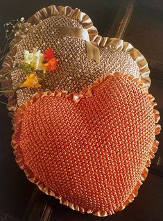 an orange heart shaped pillow sitting on top of a wooden table next to a vase with flowers