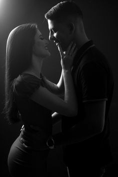 a man and woman standing next to each other in front of a spotlight light on a black background