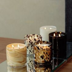 three candles sitting on top of a glass table next to another candle in front of them