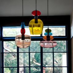 three different colored lights hanging from the ceiling in front of a window with trees outside