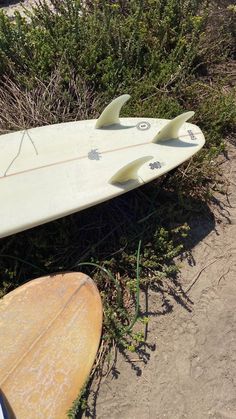 a white surfboard laying on top of a sandy beach next to bushes and shrubbery