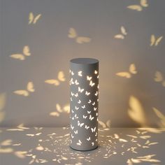 a white vase sitting on top of a table next to a wall with butterflies flying around it