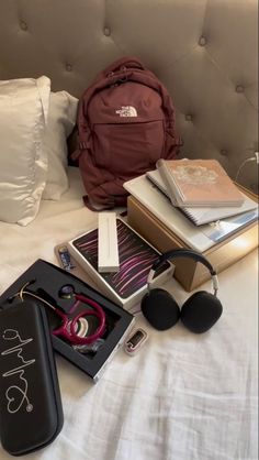 the contents of a backpack, headphones, and other items are laid out on a bed