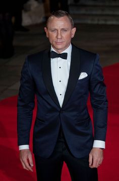 a man in a tuxedo and bow tie standing on a red carpeted area