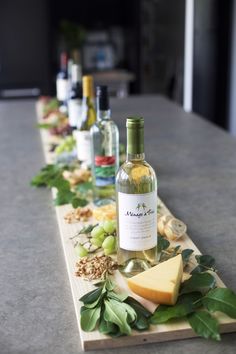 several bottles of wine and cheese are lined up on a long wooden board with leaves