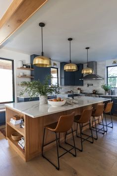 a kitchen with blue cabinets and gold pendant lights above the island countertop is surrounded by brown leather bar stools