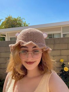 a woman wearing glasses and a crocheted hat poses in front of a house