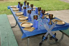 a blue table topped with lots of gold plates and silverware next to a green bench