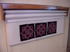 three black and pink quilts hanging on a white wall next to a wooden shelf