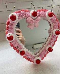 a heart shaped mirror with cherries on it and a hand holding a cell phone