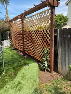 a wooden trellis on the side of a fence next to a yard with grass and flowers