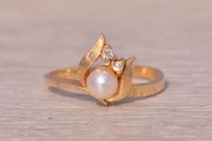 This stunning piece, known as The Moonlit Blossom, features a captivating cultured pearl at its center, beautifully accented by sparkling natural diamonds. The pearl and diamonds are set in a graceful floral motif crafted in 14-karat yellow gold, embodying elegance and sophistication. The ring is currently a finger size 6.5 but can be adjusted to any finger size for an additional charge upon request, ensuring a perfect fit. Love this piece, but don't have the money to spend right now? We offer F Elegant Pearl Ring With Rose Cut Diamonds For Anniversary, Wedding Pearl Drop Ring With Diamond, Wedding Pearl Ring With Single Diamond, Wedding Pearl Ring With Diamond, Wedding Pearl Ring With Diamond Accents And Akoya Pearl, Fine Jewelry Pearl Ring With Single Diamond For Wedding, Elegant Pearl Ring With Single Cut Diamonds, Elegant Diamond Ring With Pearl Drop For Anniversary, Wedding Akoya Pearl Ring With Diamond Accents