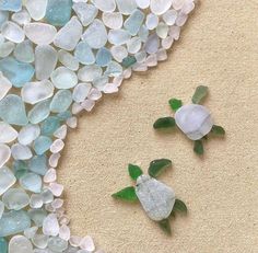 two sea glass turtles sitting on the sand next to each other with green leaves sticking out of them