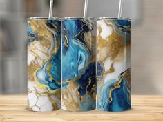 three tumbles with gold, blue and white designs on them sitting on a wooden table