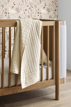 a crib with a blanket on top of it next to a wallpapered wall