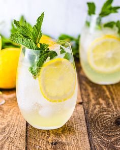 two glasses filled with lemonade and mint garnish on top of a wooden table