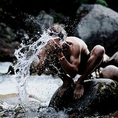 a shirtless man splashing water on rocks in the river