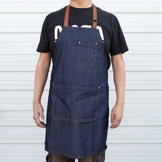 a man wearing an apron and black t - shirt stands in front of a garage door