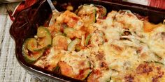 a casserole dish with cheese and vegetables in it on a tablecloth next to a fork