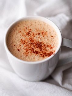 a cup of coffee with cinnamon sprinkles in it on a white blanket