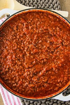 a large pot filled with chili sauce on top of a wooden table next to a red and white towel