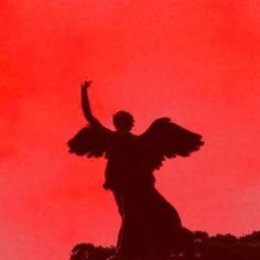 the silhouette of an angel with outstretched arms against a red sky background, in front of a black statue