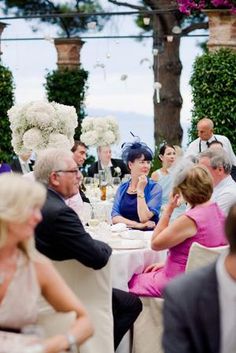 a group of people sitting at tables with white flowers on top of them and wine glasses in front of them