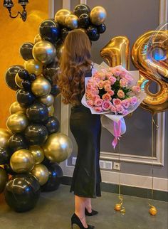 a woman is standing in front of balloons and holding a bouquet of flowers with the number 3 on it