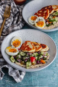 two white bowls filled with food on top of a blue tablecloth next to a fork