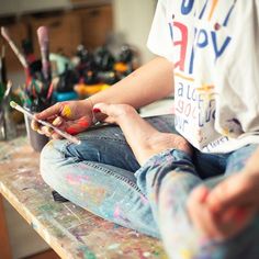 a person sitting on top of a table holding a smart phone and painting with paint