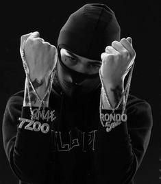 a man wearing a black hoodie with chains around his neck and hands behind his head