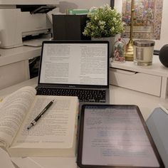 an open laptop computer sitting on top of a desk next to a book and pen