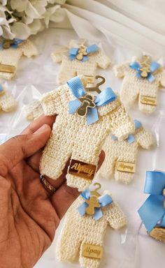 a hand holding a crocheted teddy bear with blue ribbon around it and other small ones in the background