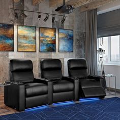 three black recliner chairs in front of a wall with paintings on it and a blue rug