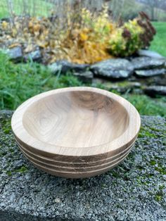 a wooden bowl sitting on top of a stone wall next to grass and flowers in the background