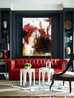 a living room filled with furniture and a painting on the wall above it's red couch