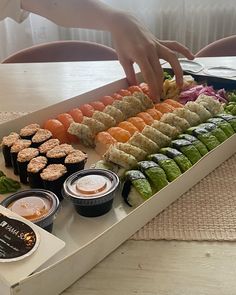 sushi platter being served with dipping sauces on the side and someone reaching for it