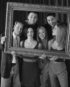 a group of people standing around each other in front of a photo booth holding up a frame