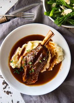 a plate with mashed potatoes, meat and gravy next to a bowl of broccoli