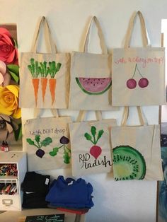 tote bags hanging up on the wall with fruit and vegetables painted on them,