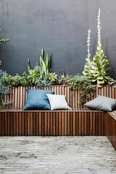 a wooden bench sitting next to a wall with plants growing on it and two blue pillows