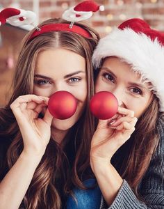 two young women wearing santa hats holding red balls