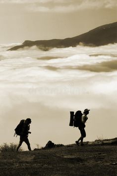 two people with backpacks walking up a hill above the clouds in black and white