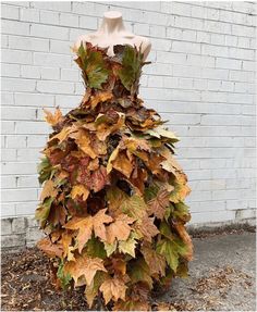 a dress made out of leaves sitting in front of a brick wall