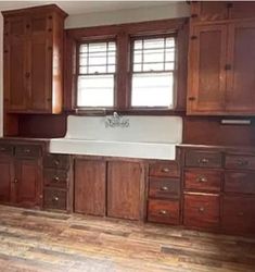 an empty kitchen with wooden cabinets and white sink in the center, wood flooring