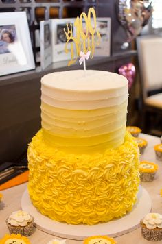 a yellow and white cake sitting on top of a table next to cupcakes