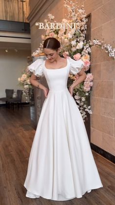 a woman wearing a white dress standing in front of a wall with flowers on it