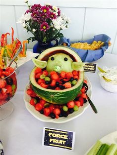 a watermelon sculpture made to look like a baby yoda in a fruit bowl