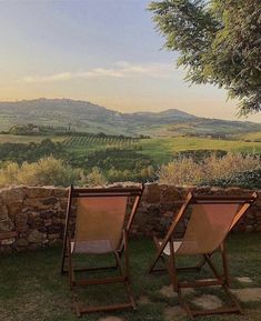 two lawn chairs sitting next to each other on top of a grass covered field with mountains in the background