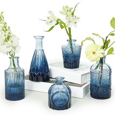 blue glass vases with flowers in them sitting on a white book and some books